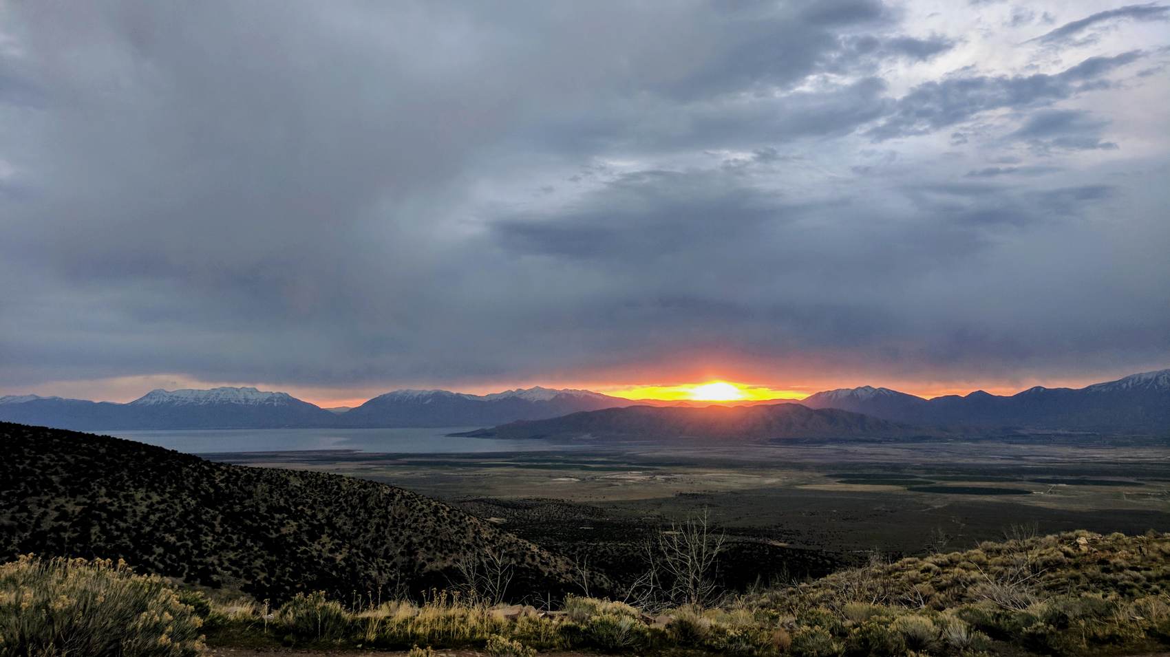 Sun breaking through storm clouds over mountains and a valley lake